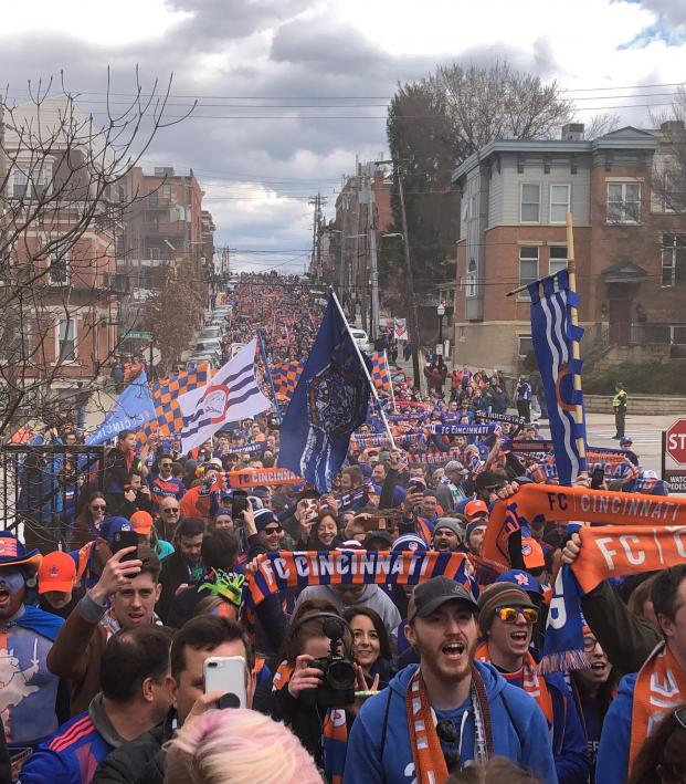 a crowd of FC Cincinnati soccer fans marching towards the stadium to attend a match