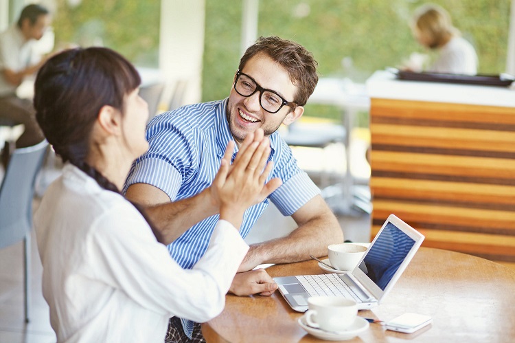 two smiling coworkers high-fiving each other in a coffee shop