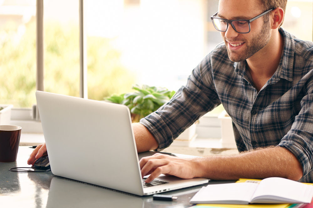 a smiling man typing on his laptop